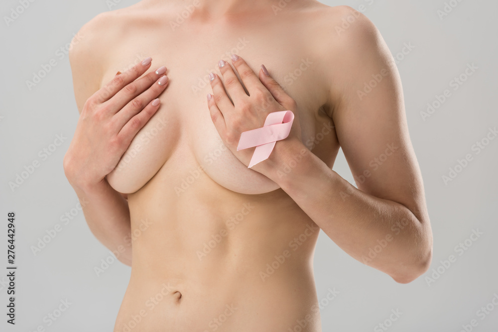 partial view of topless young woman with pink ribbon covering breast isolated on grey partial view of topless young woman with pink ribbon covering breast isolated on grey