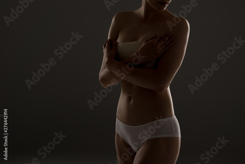 cropped view of woman in panties with breast bandage in darkness photo