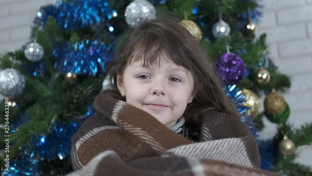 Frosty Christmas evening. Beautiful little girl at the Christmas tree wrapped in a blanket. Frosty Christmas evening. Beautiful little girl at the Christmas tree wrapped in a blanket.
