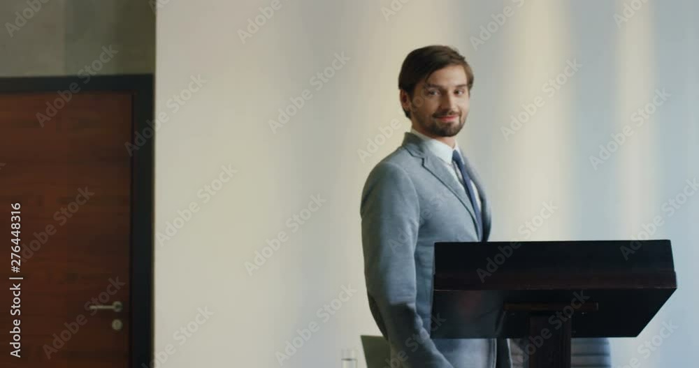 Back view on the Caucasian famous handsome man, business coach, walking among the sitting audience to the podium, then turning and smiling. Back view on the Caucasian famous handsome man, business coach, walking among the sitting audience to the podium, then turning and smiling.