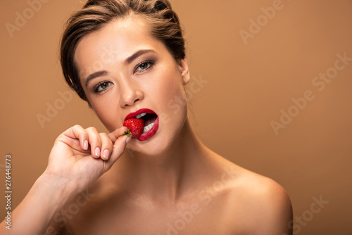 naked beautiful woman biting strawberry isolated on beige