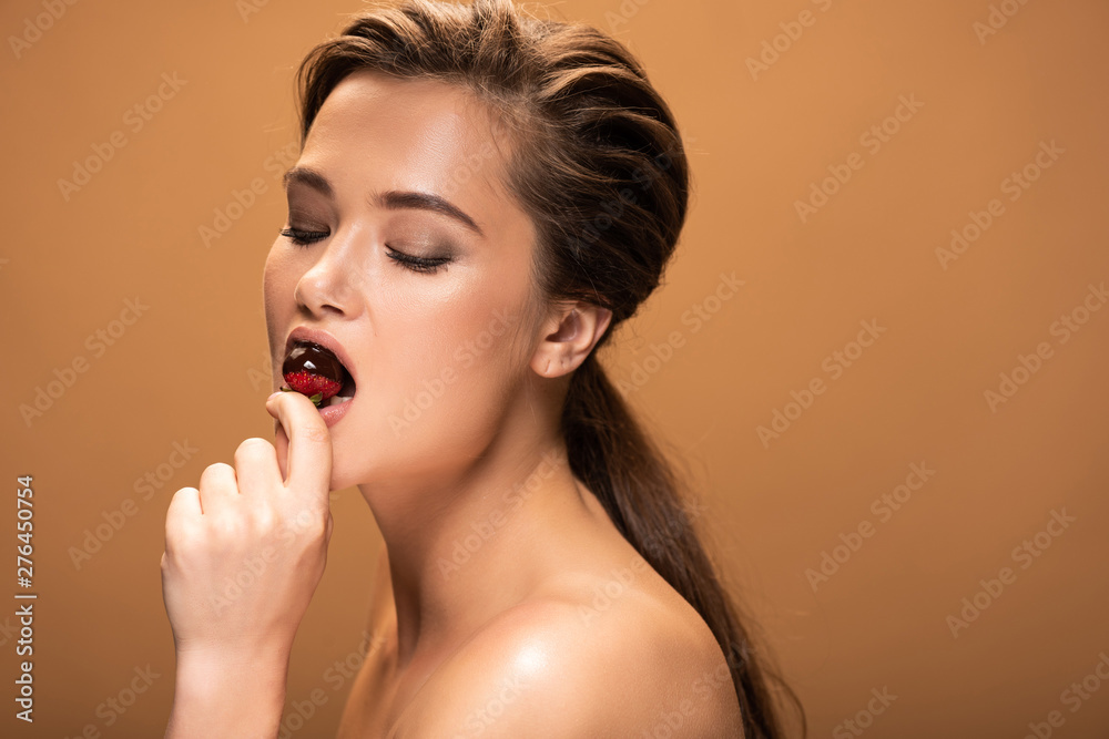 beautiful nude woman with closed eyes eating strawberry in melted chocolate isolated on beige