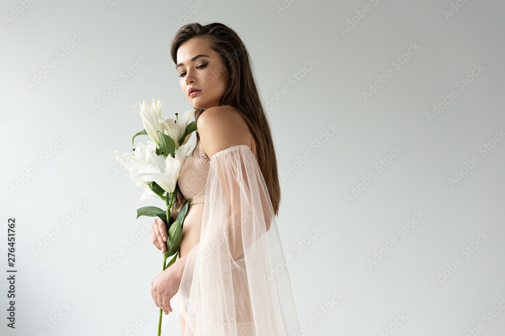 sexy tender young woman in beige lingerie and mesh sleeves holding lilies isolated on white sexy tender young woman in beige lingerie and mesh sleeves holding lilies isolated on white