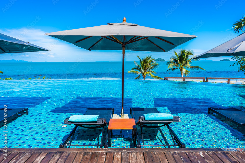 Fototapeta premium Beautiful luxury outdoor swimming pool in hotel resort with sea ocean around coconut palm tree and white cloud on blue sky