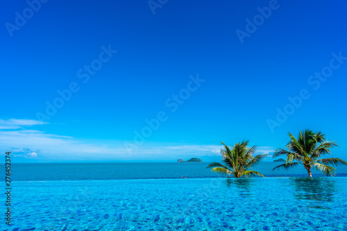 Beautiful luxury outdoor swimming pool in hotel resort with sea ocean around coconut palm tree and white cloud on blue sky