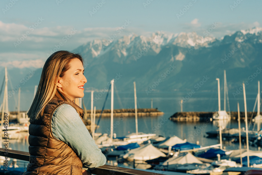 Outdoor fashion portrait of beautiful young woman posing by the lake in a small port