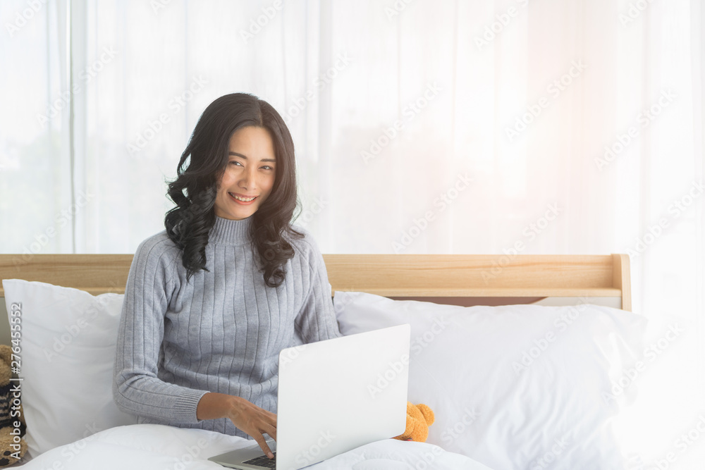 Asian woman sitting and using laptop in bedroom. . Asian woman sitting and using laptop in bedroom. .