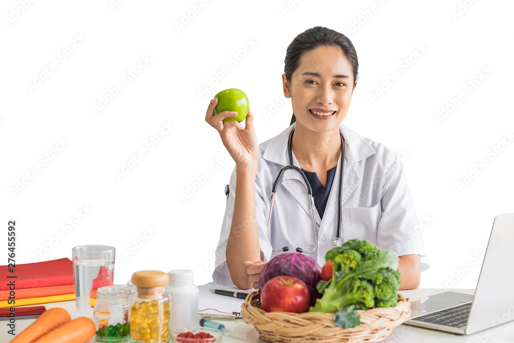 A young woman doctor nutritionist smiling siting working on her laptop in her office holding green apple in front of isolated white background. A young woman doctor nutritionist smiling siting working on her laptop in her office holding green apple in front of isolated white background.
