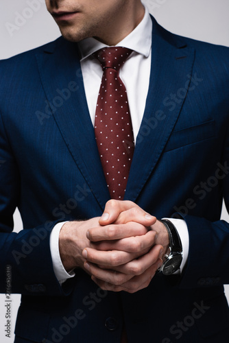 partial view of confident businessman standing with clenched hands isolated on grey, human emotion and expression concept
