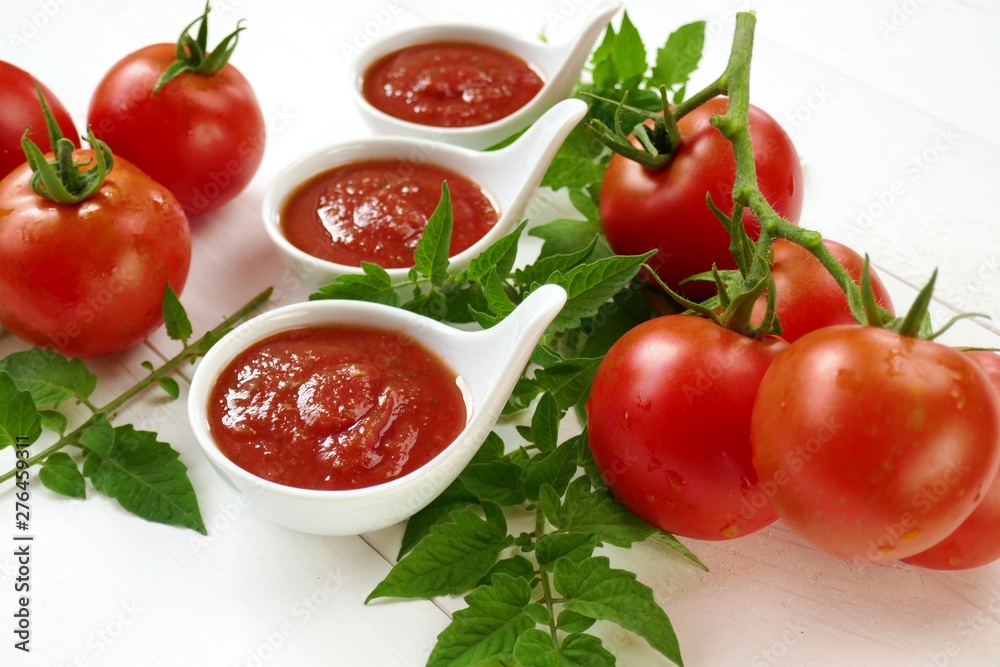 Tomato Sauce.Homemade tomato sauce in a white sauce pan set and fresh ripe tomatoes with leaves on a white wooden background. Tomato Sauce.Homemade tomato sauce in a white sauce pan set and fresh ripe tomatoes with leaves on a white wooden background.