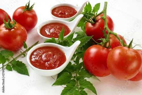 Tomato Sauce.Homemade tomato sauce in a white sauce pan set and fresh ripe tomatoes with leaves on a white wooden background.