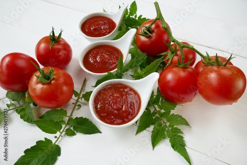 Tomato Sauce.Homemade tomato sauce in a white sauce-pan set and fresh ripe tomatoes with leaves on a white background.