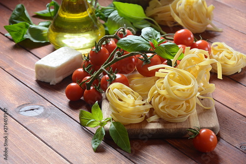 Concept of Italian food with raw pasta, tomato, basil and oil, selective focus 
