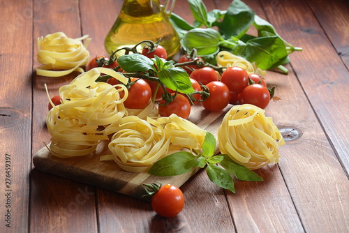 Concept of Italian food with raw pasta, tomato, basil and oil, selective focus 