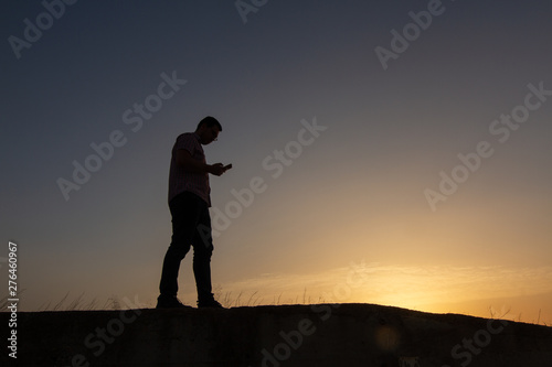 silhouette of man with cell phone at sunset