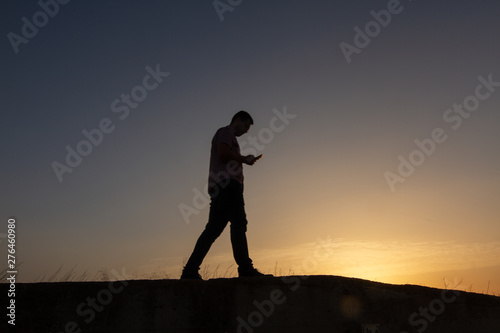 silhouette of man with cell phone at sunset