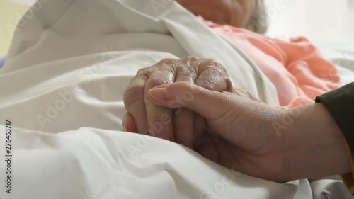 taking care of elderly person confined to bed,family member holding old hand, strong emotional scene photo