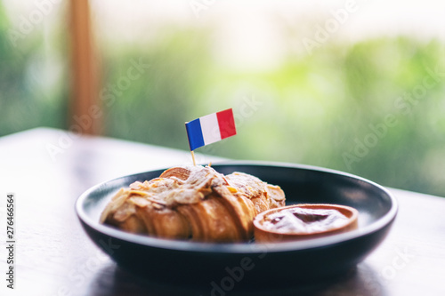 A piece of croissant and tart with a flag of France in a black plate on wooden table in cafe
