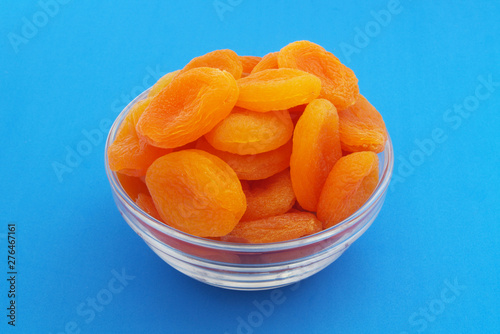 Heap of dried apricots fruits in bowl on blue background