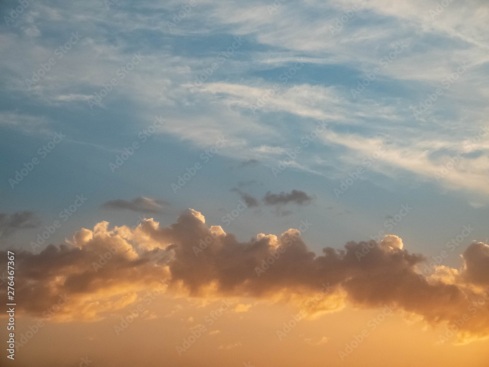 Bright multicolored clouds enlightened with rays of setting sun. Bright blue sky with orange cumulus, stratus and cirrus clouds