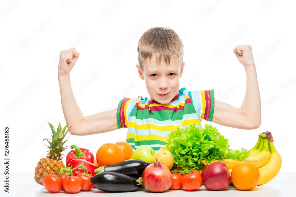 small strongman shows biceps at the table with a pile of fresh vegetables and fruits isolated in the studio small strongman shows biceps at the table with a pile of fresh vegetables and fruits isolated in the studio