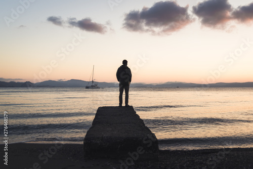 A man standing on a dock during sunrise on Kos, Greece with a boat in the background. 