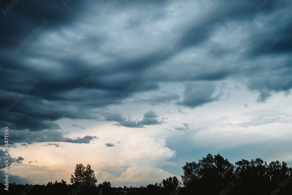 Dramatic cloudscape. Sunny light through dark heavy thunderstorm clouds before rain. Overcast rainy bad weather. Storm warning. Natural blue background of cumulonimbus. Sunlight in stormy cloudy sky.