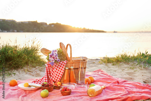 Wicker basket with tasty food and drink for romantic picnic near river