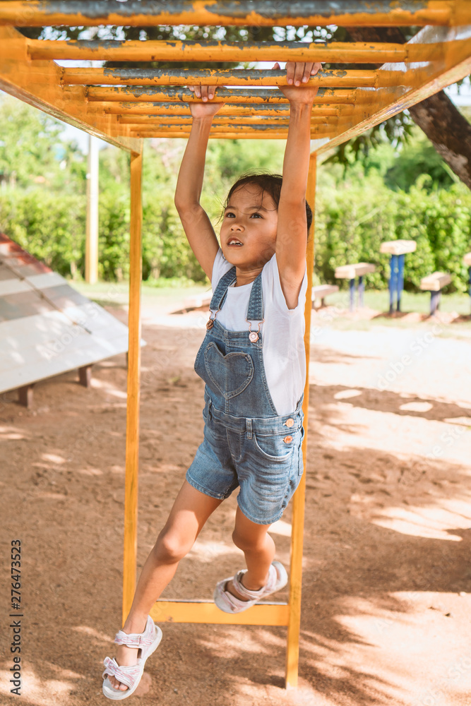 Cute asian child girl hang the bar by her hand to exercise in the playground with fun and strong Cute asian child girl hang the bar by her hand to exercise in the playground with fun and strong