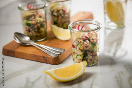 Norddeutscher Friesischer Nordseekrabben Salat Glas Becher mit Gurken, Radieschen, Zwiebeln, Dill und Zitronen auf Holz Brett und Marmor Tisch