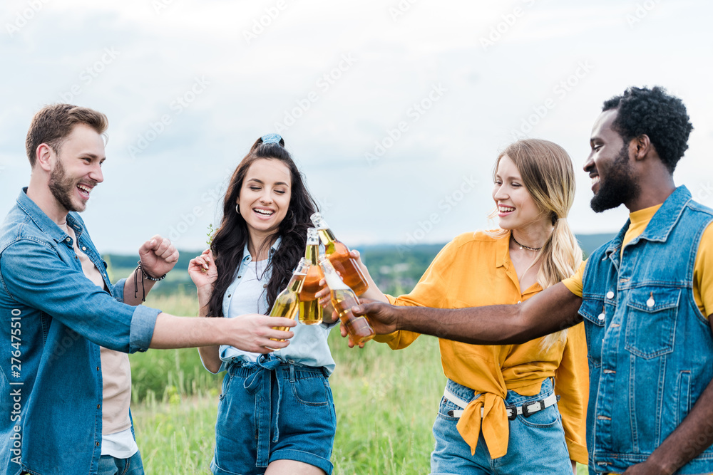 happy multicultural men and women clinking bottles with beer happy multicultural men and women clinking bottles with beer
