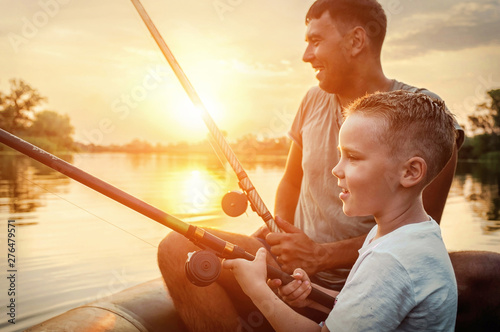 Happy Father and Son together fishing from a boat at sunset time photo