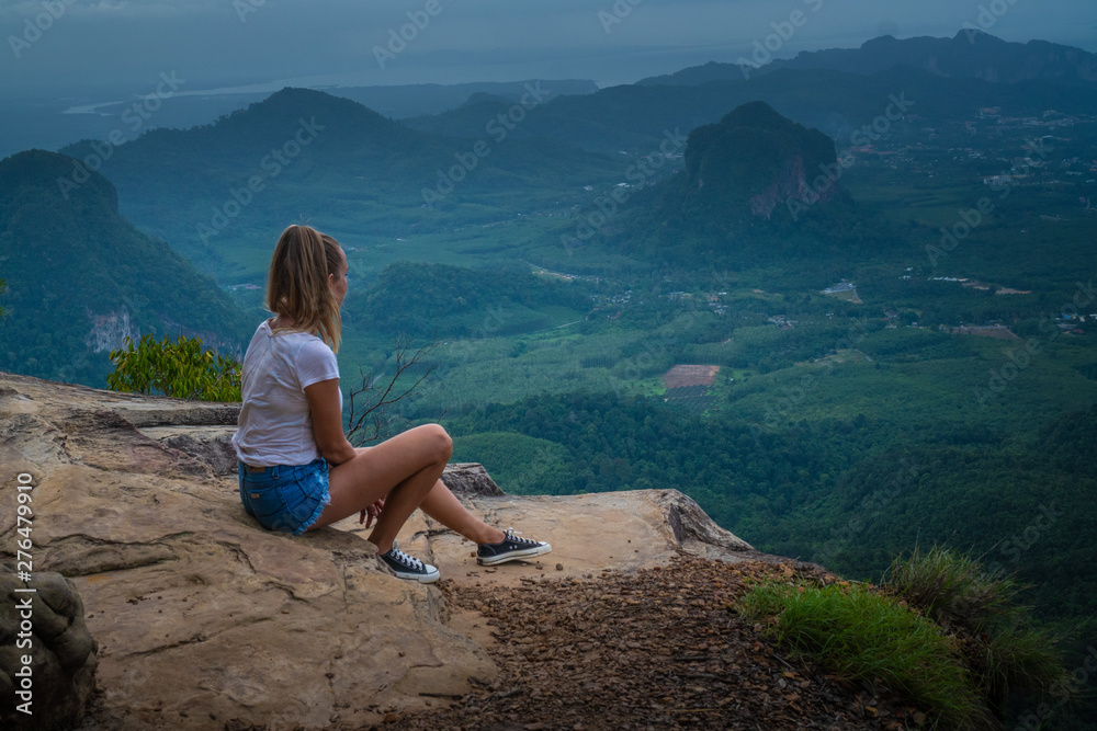 Naklejka premium Woman taveler sitting on the cliff and looking at the beautiful landscape with mountains and valley with cloudy morning sky