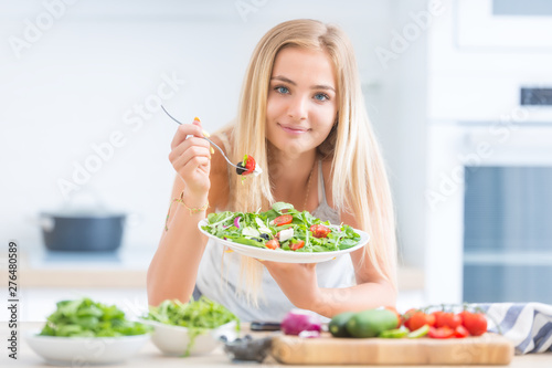 Young happy blonde girl eating healthy salad from arugula spinach tomatoes olives onion and olive oil