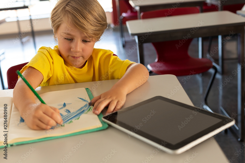 Boy drawing sketch on notebook at desk in a classroom Boy drawing sketch on notebook at desk in a classroom