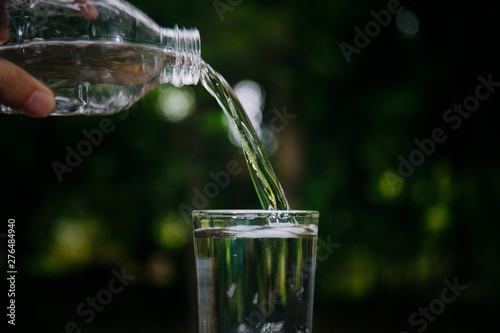 Drinking water pouring from bottle into glass on blurred green nature background