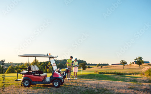 Woman and her partner or instructor holding various golf clubs near golf cart