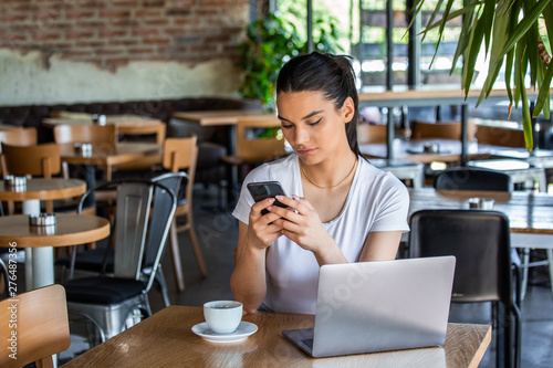 Young woman with coffee cup and laptop talking on her smart phone. Woman taking a break. Doing Business From the coffee shop