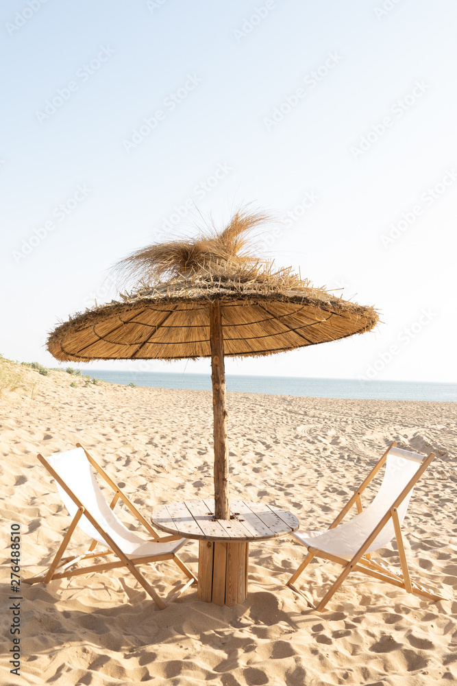 table et chaises longues sous parasol en paille sur la plage devant le front de mer