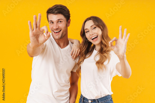 Portrait of joyful couple man and woman in basic t-shirts rejoicing and showing ok sign at camera