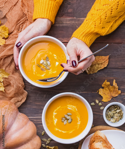 Woman's hands holding table sppoon near the bowl of delecious homemade pumpkin soup with cream on the wooden table top view