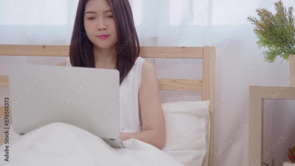 Young business freelance Asian woman working on laptop checking social media while lying on the bed when relax in bedroom at home. Lifestyle women at house concept. Young business freelance Asian woman working on laptop checking social media while lying on the bed when relax in bedroom at home. Lifestyle women at house concept.