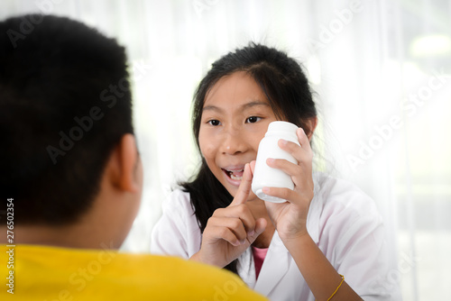 Asian girl pharmacist explaining something to a preteen boy, holding blisters with pills, health care concept.