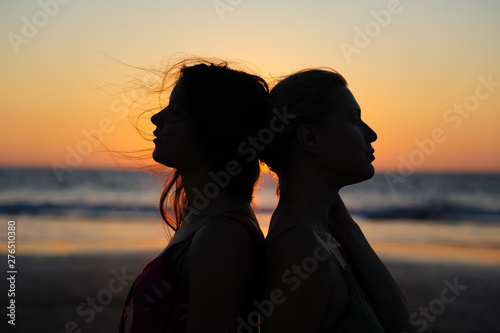 Close up silhouette of womens couple in romantic scene of sunset over the sea. Beautiful female young lesbian couple in love.