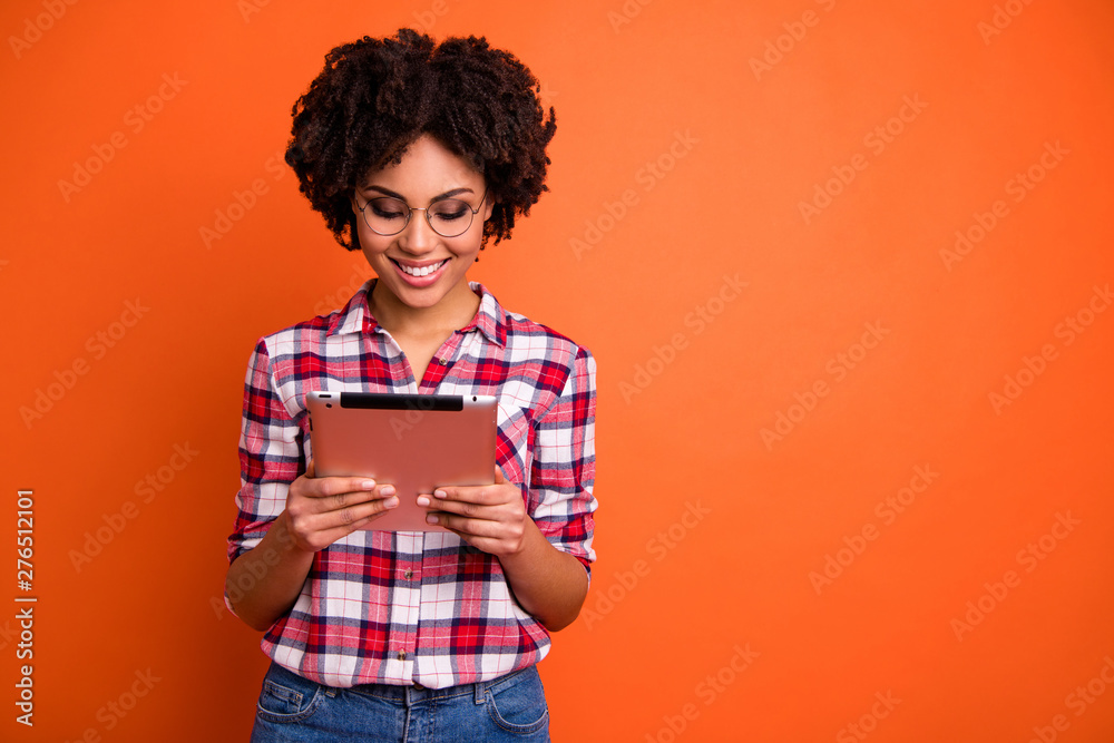 Portrait of nice cute attractive cheerful cheery smart clever intellectual wavy-haired lady nerd wearing checked shirt reading digital e-book isolated over bright vivid shine orange background Portrait of nice cute attractive cheerful cheery smart clever intellectual wavy-haired lady nerd wearing checked shirt reading digital e-book isolated over bright vivid shine orange background