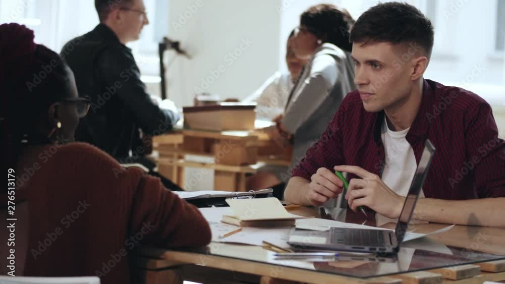 Happy smiling young Caucasian male business manager talking to African female colleague at modern office table.