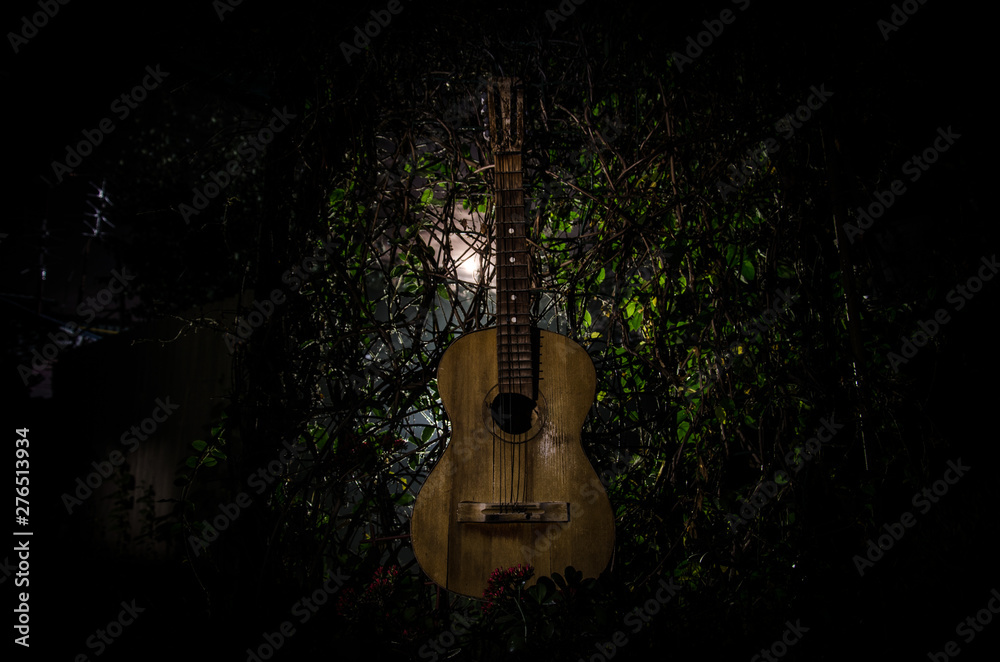 Fototapeta An wooden acoustic guitar is against a grunge textured wall. The room is dark with a spotlight for your copyspace.