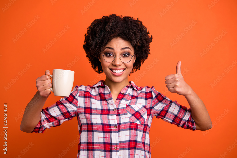 Close up photo of model wavy lady hold hands hot beverage mug thumb up symbol morning wear casual checkered plaid shirt isolated orange background