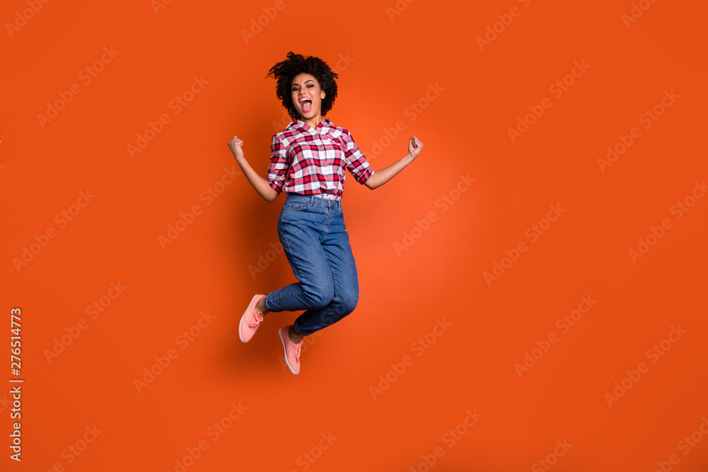 Full size photo of excited crazy jumping high lady yelling yeah raise fists wear jeans denim pants plaid shirt outfit isolated orange background