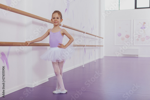 Full length shot of a lovely little ballerina girl wearing violet leotard and tutu dancing ballet at dance class, copy space. Graceful little girl practicing ballet